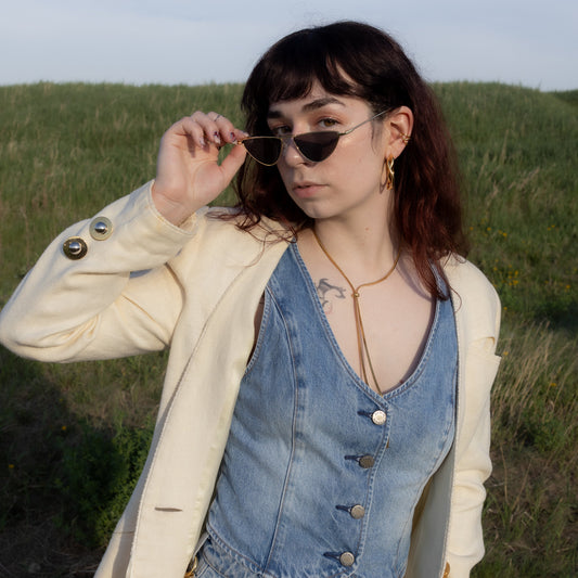 Woman wearing a denim dress and beige jacket in a grassy field