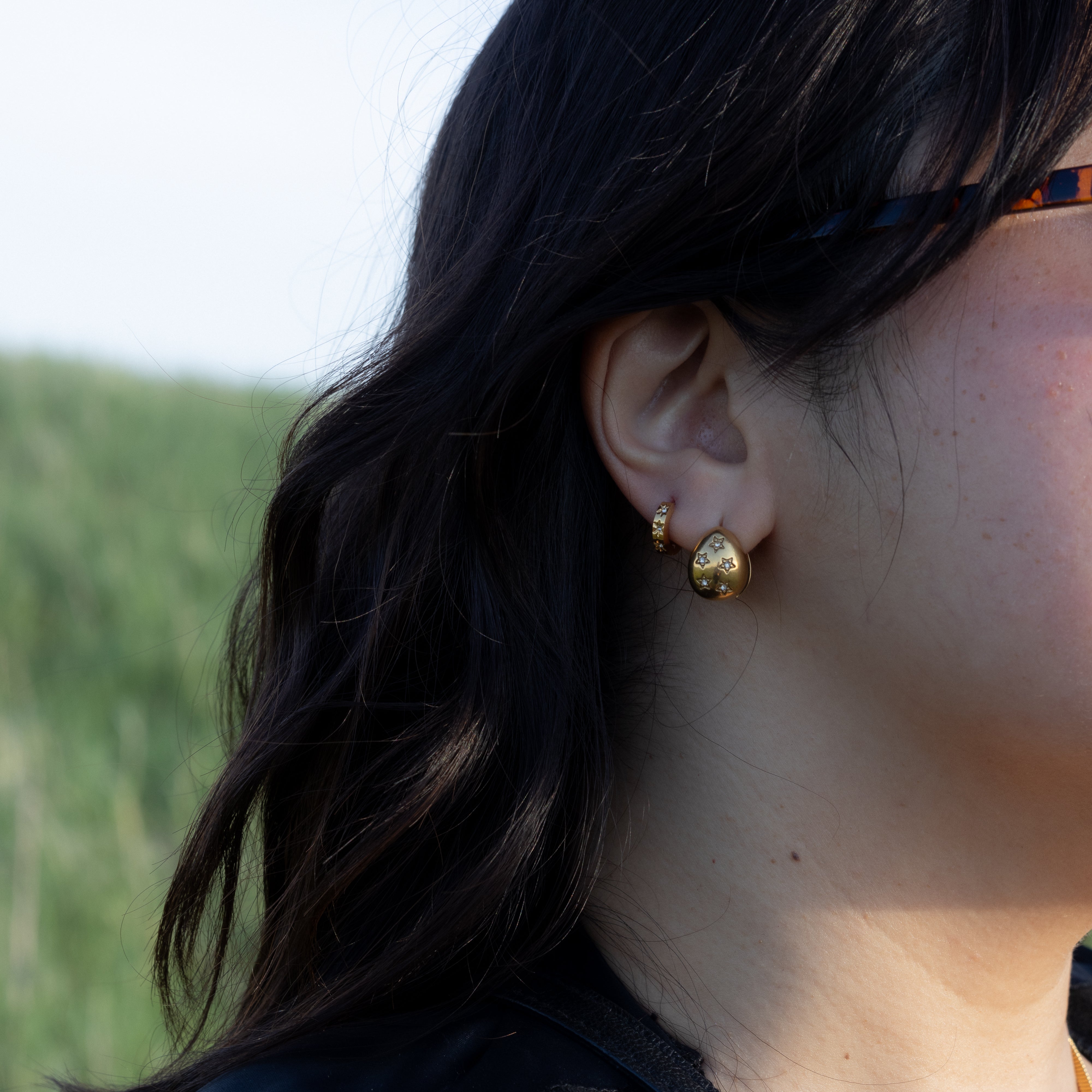 Close-up of a person wearing gold earrings with a blurred natural background