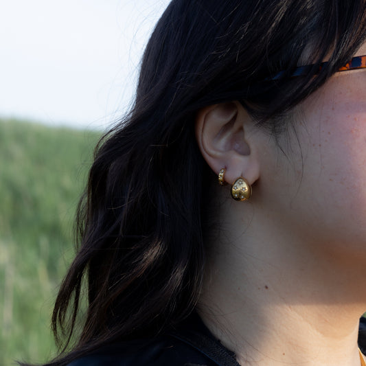 Close-up of a person wearing gold earrings with a blurred natural background