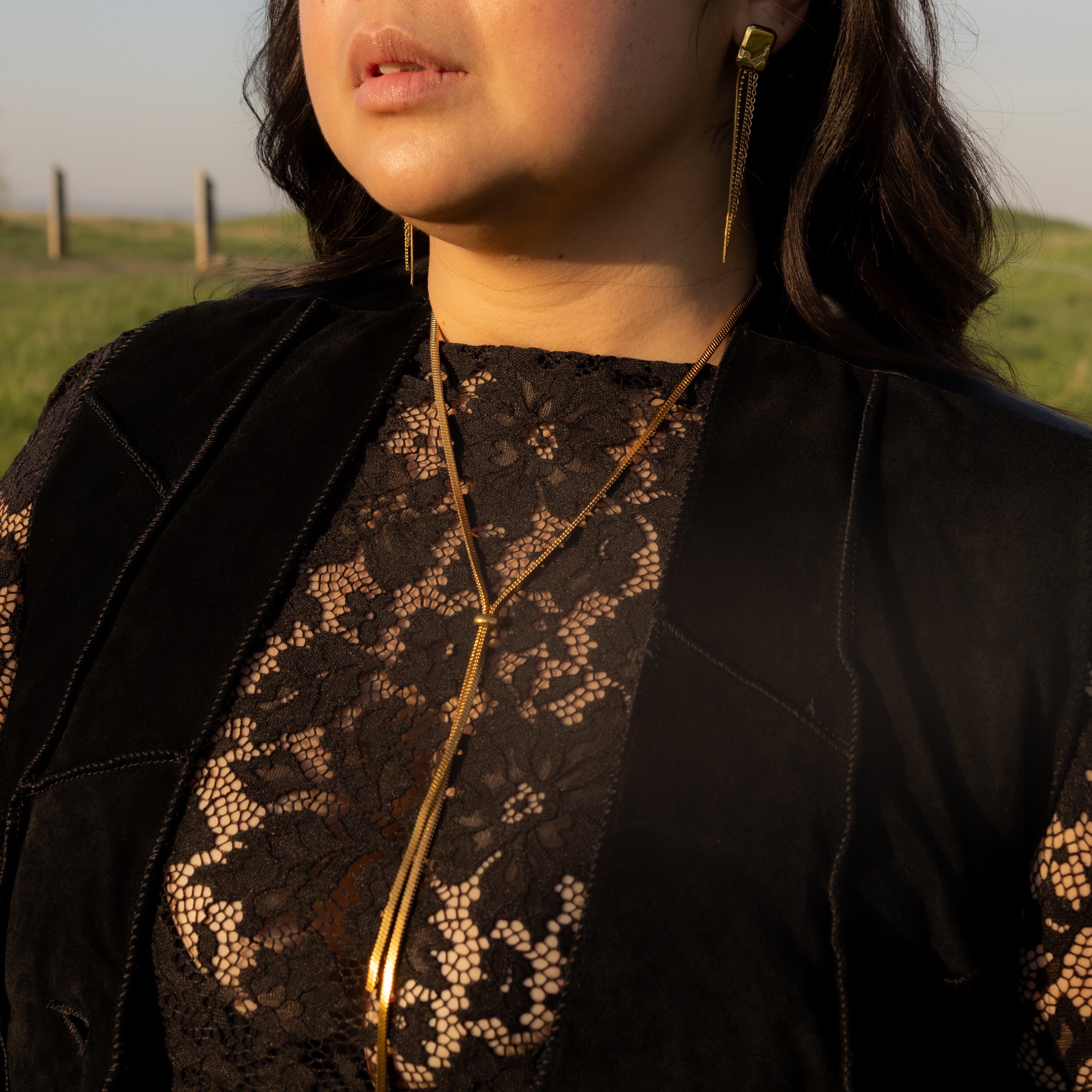 Woman wearing sunglasses and a black outfit with gold accents outdoors