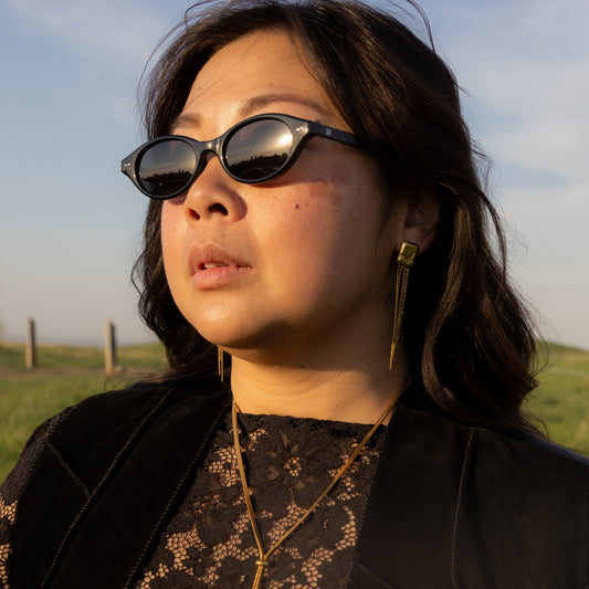 Woman wearing sunglasses and a black outfit with gold accents outdoors