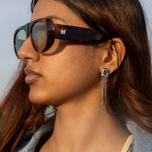 Woman wearing sunglasses and a denim jacket with a colorful top, against a light blue background
