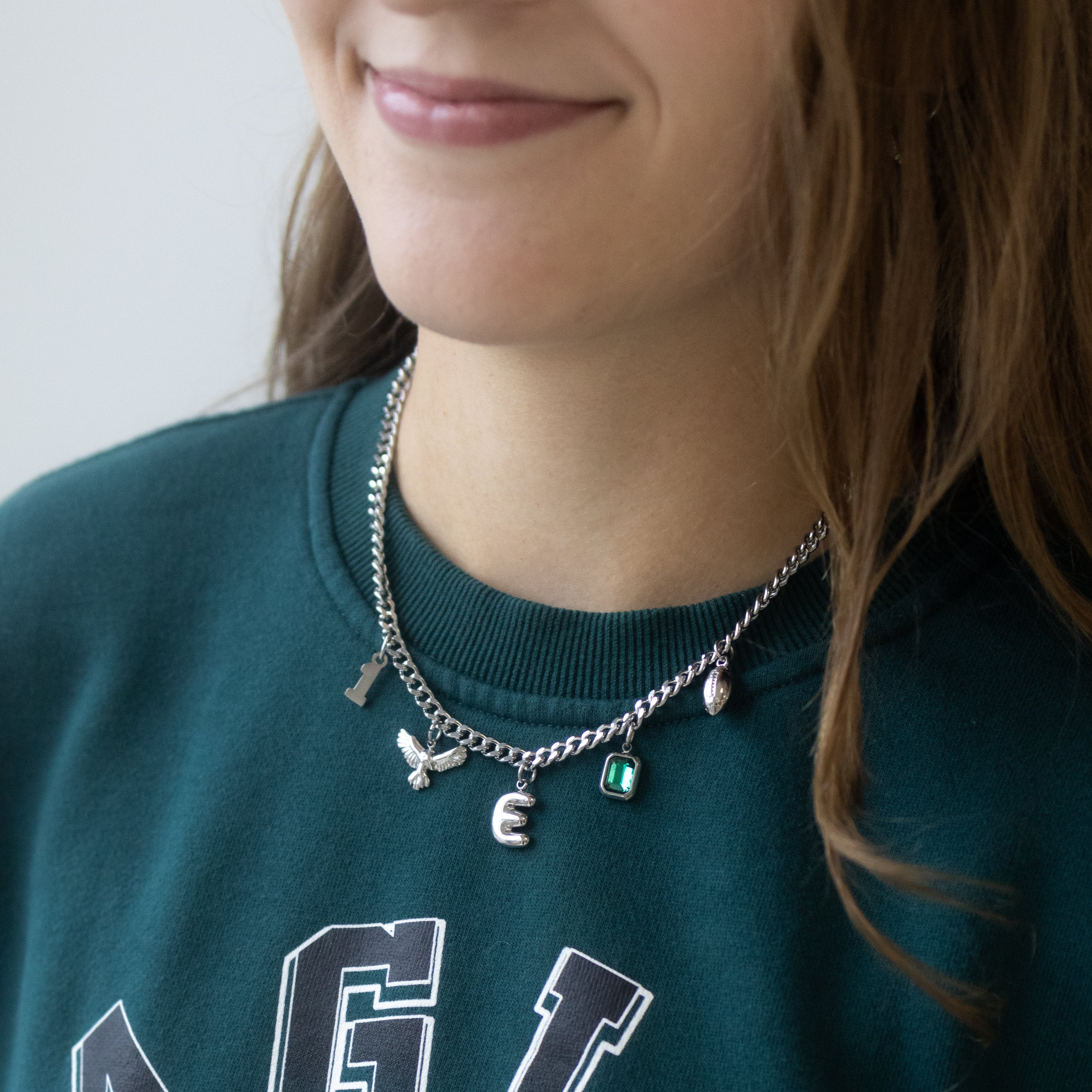 A close-up of a person wearing a silver-toned charm necklace with Eagles-themed charms, paired with a dark green Philadelphia Eagles sweatshirt.