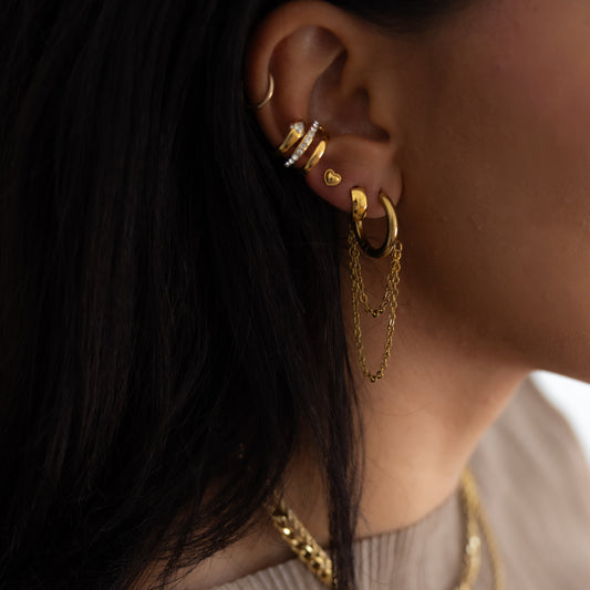 Close-up of an ear with gold earrings and necklaces against a neutral background