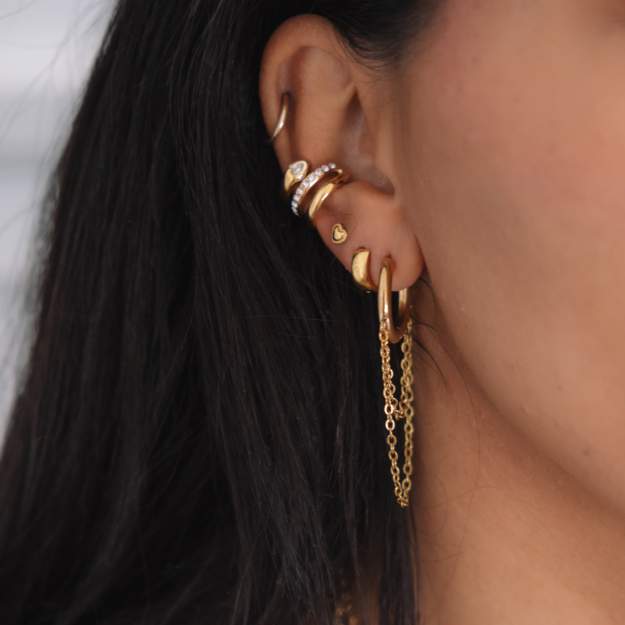 Close-up of an ear with gold earrings and a chain accessory.