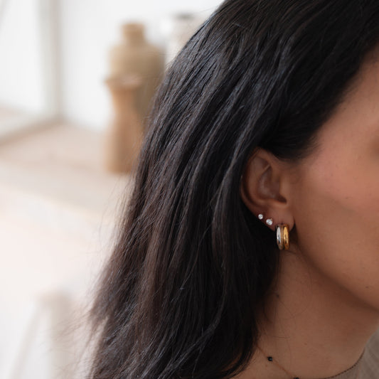 Close-up of a person with long dark hair wearing gold hoop earrings in a blurred indoor setting.