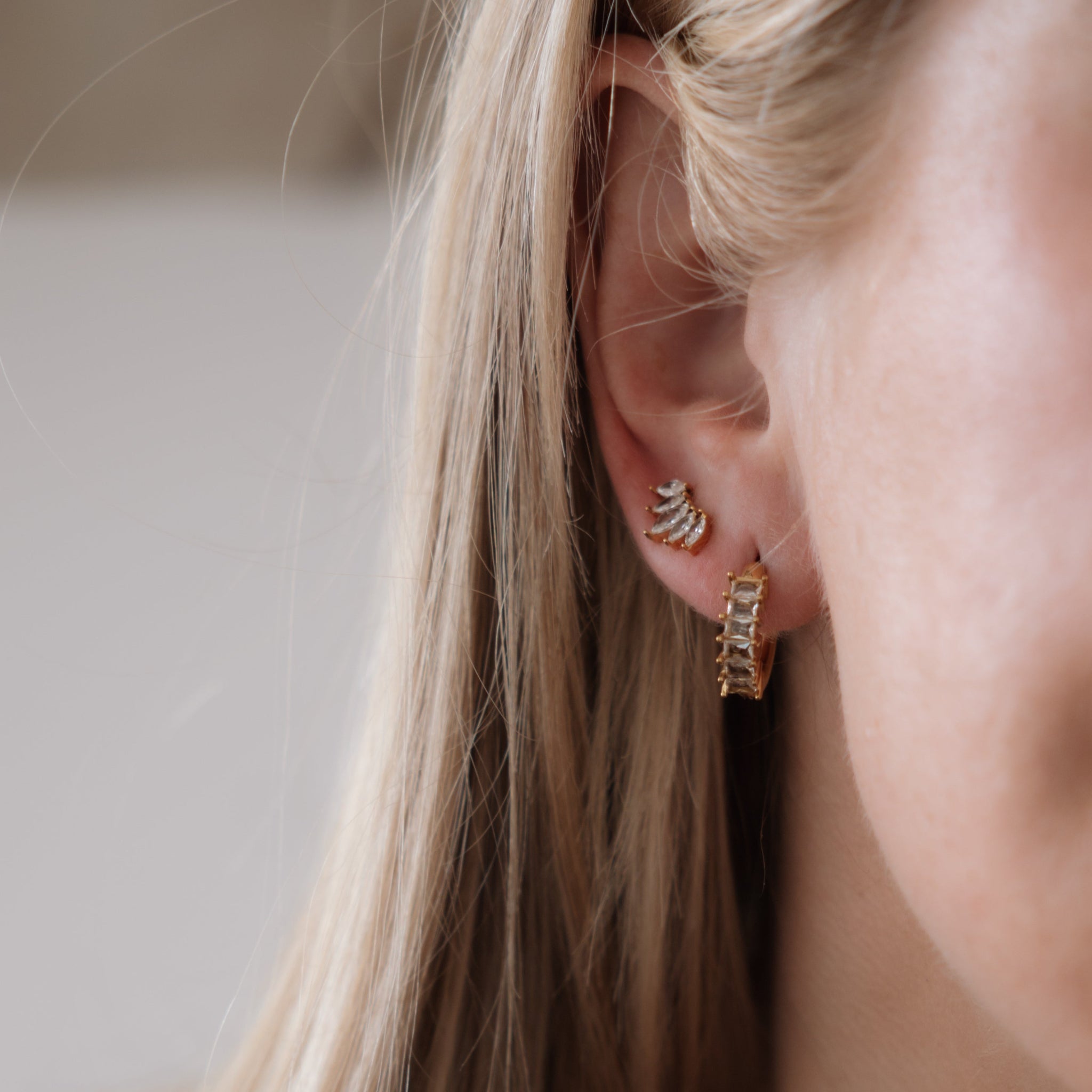 Close-up of a person wearing gold hoop earrings with a neutral background