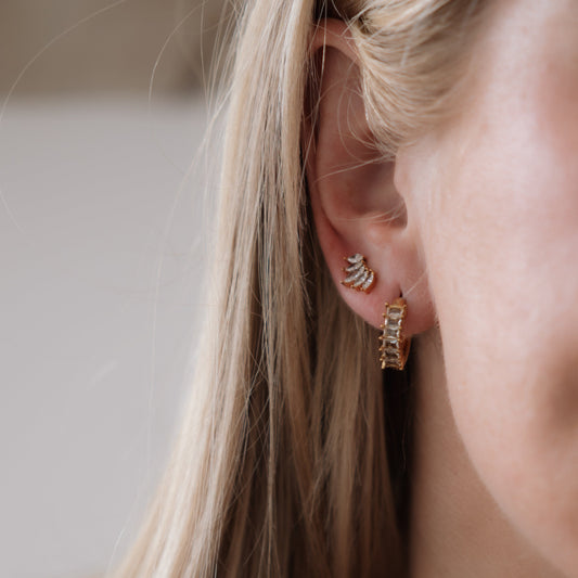 Close-up of a person wearing gold hoop earrings with a neutral background