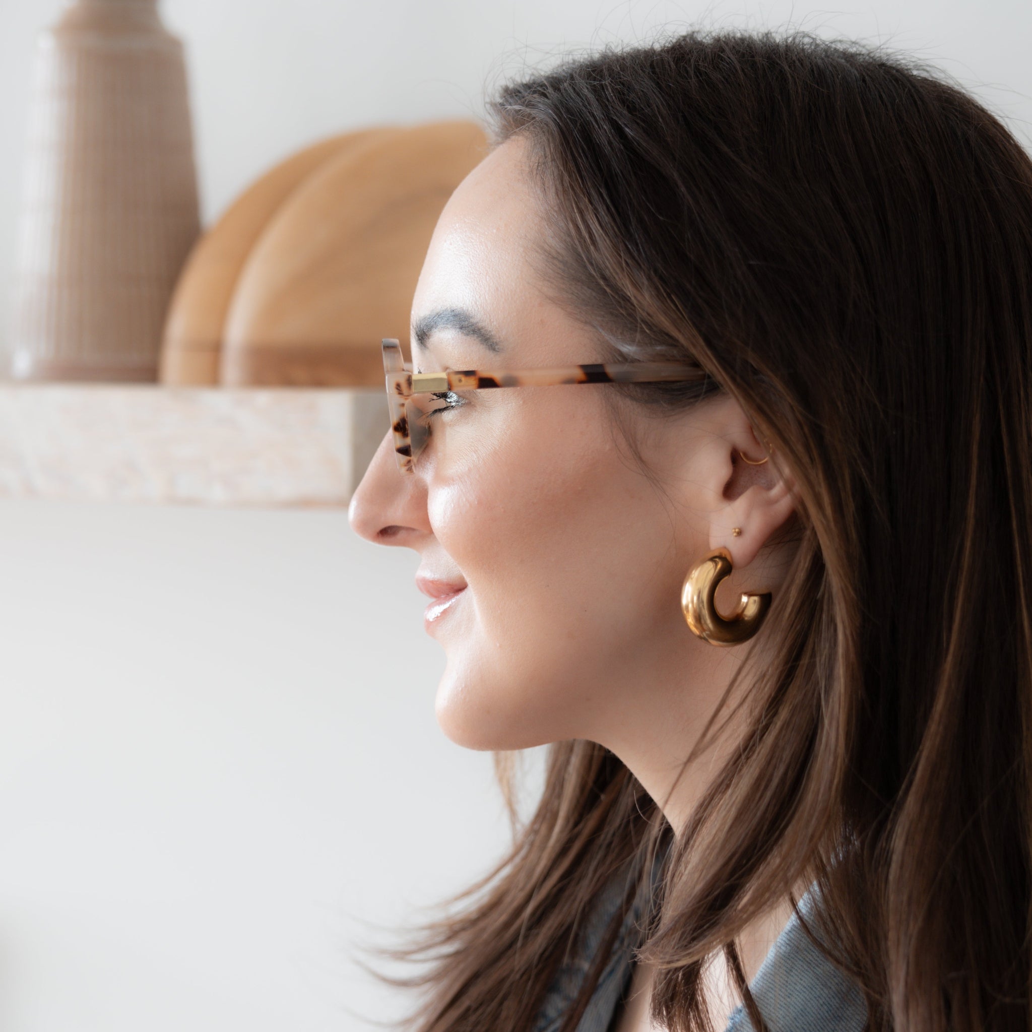 Woman wearing glasses and gold hoop earrings, with a blurred indoor background