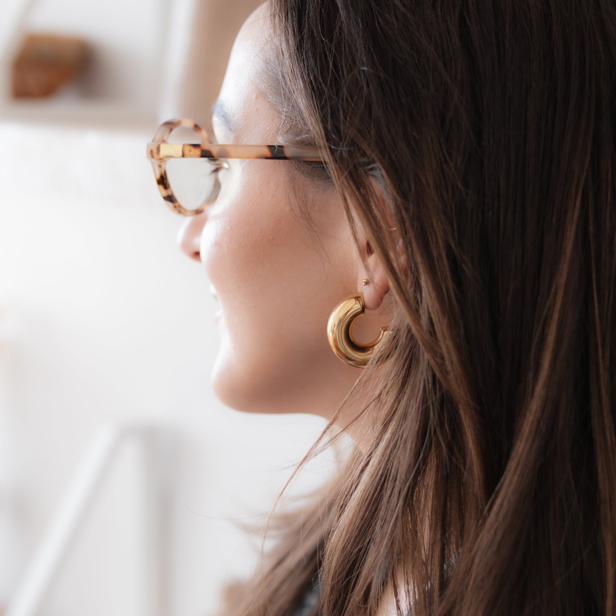 Woman wearing gold hoop earrings and glasses, with a blurred indoor background