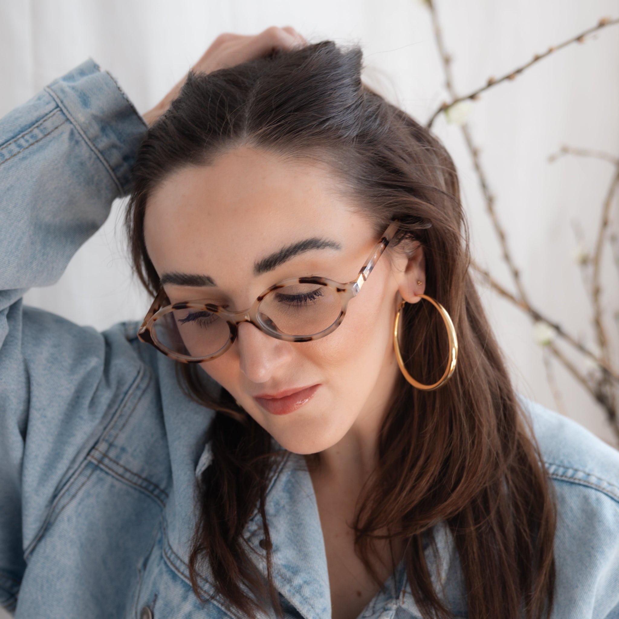 Woman wearing glasses and a denim jacket with big hoop earrings