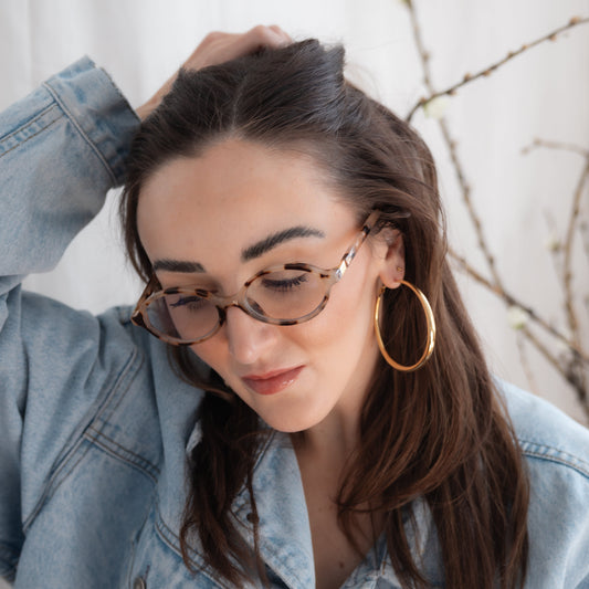 Woman wearing glasses and a denim jacket with big hoop earrings
