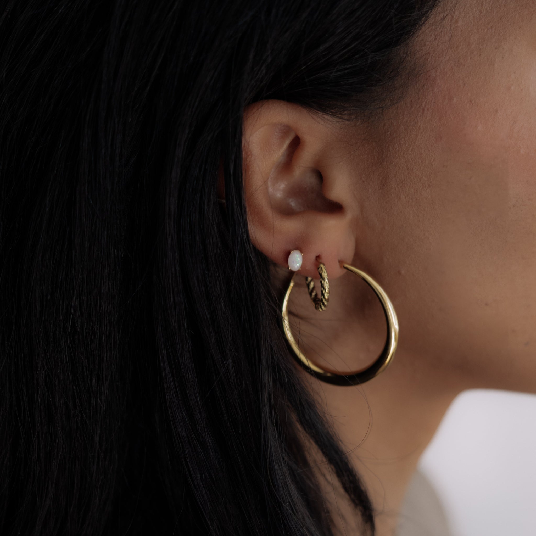 Close-up of a person wearing gold hoop earrings and opal stud