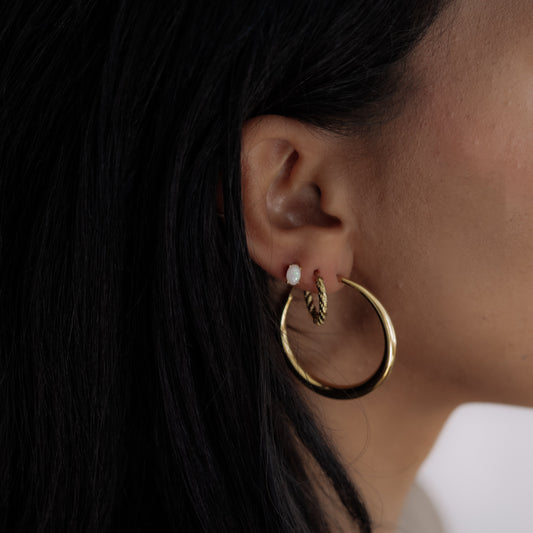 Close-up of a person wearing gold hoop earrings with a blurred background