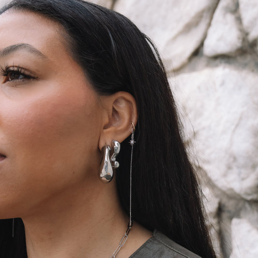 Woman wearing silver earrings and a necklace against a stone wall.