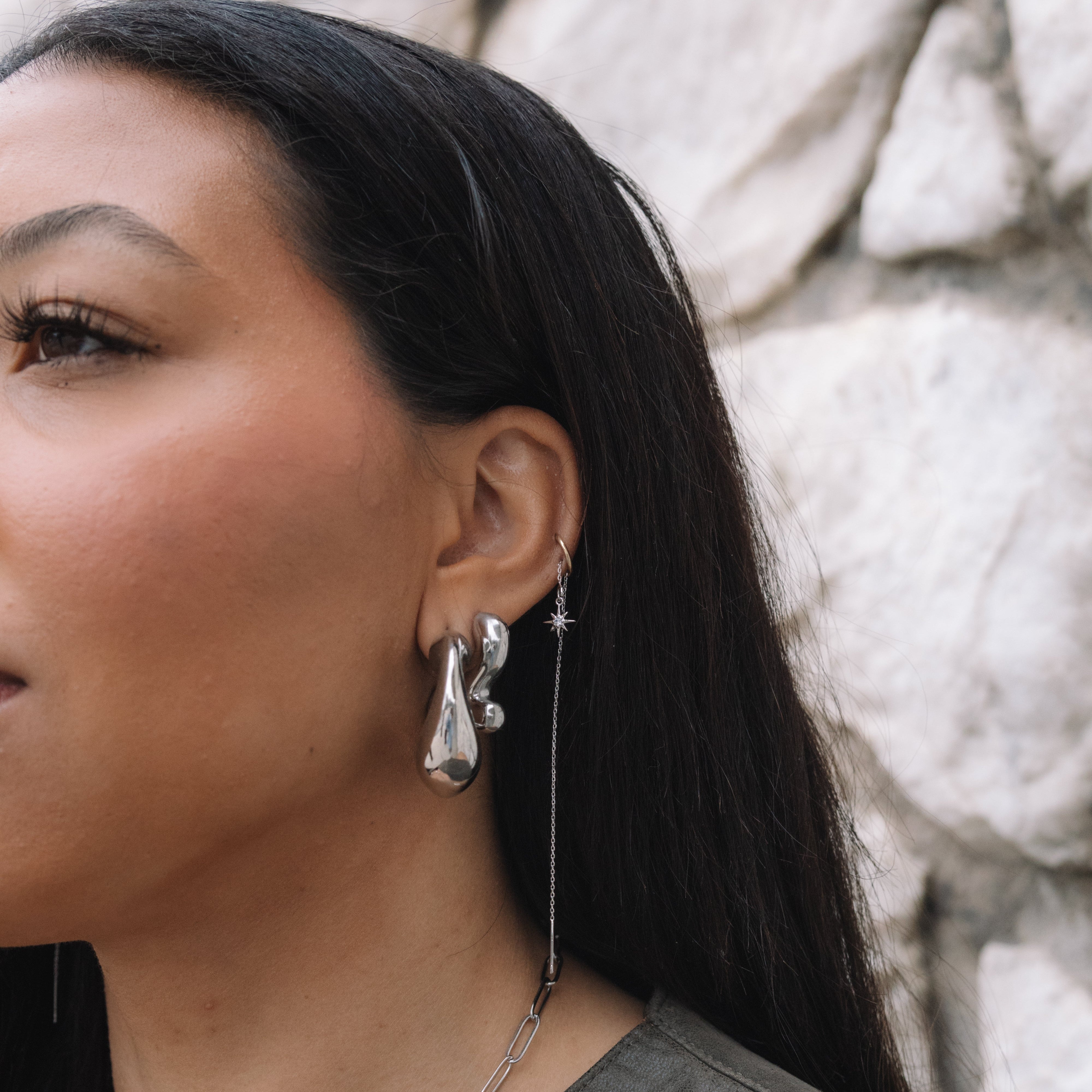 Woman wearing silver earrings and a necklace against a stone wall.