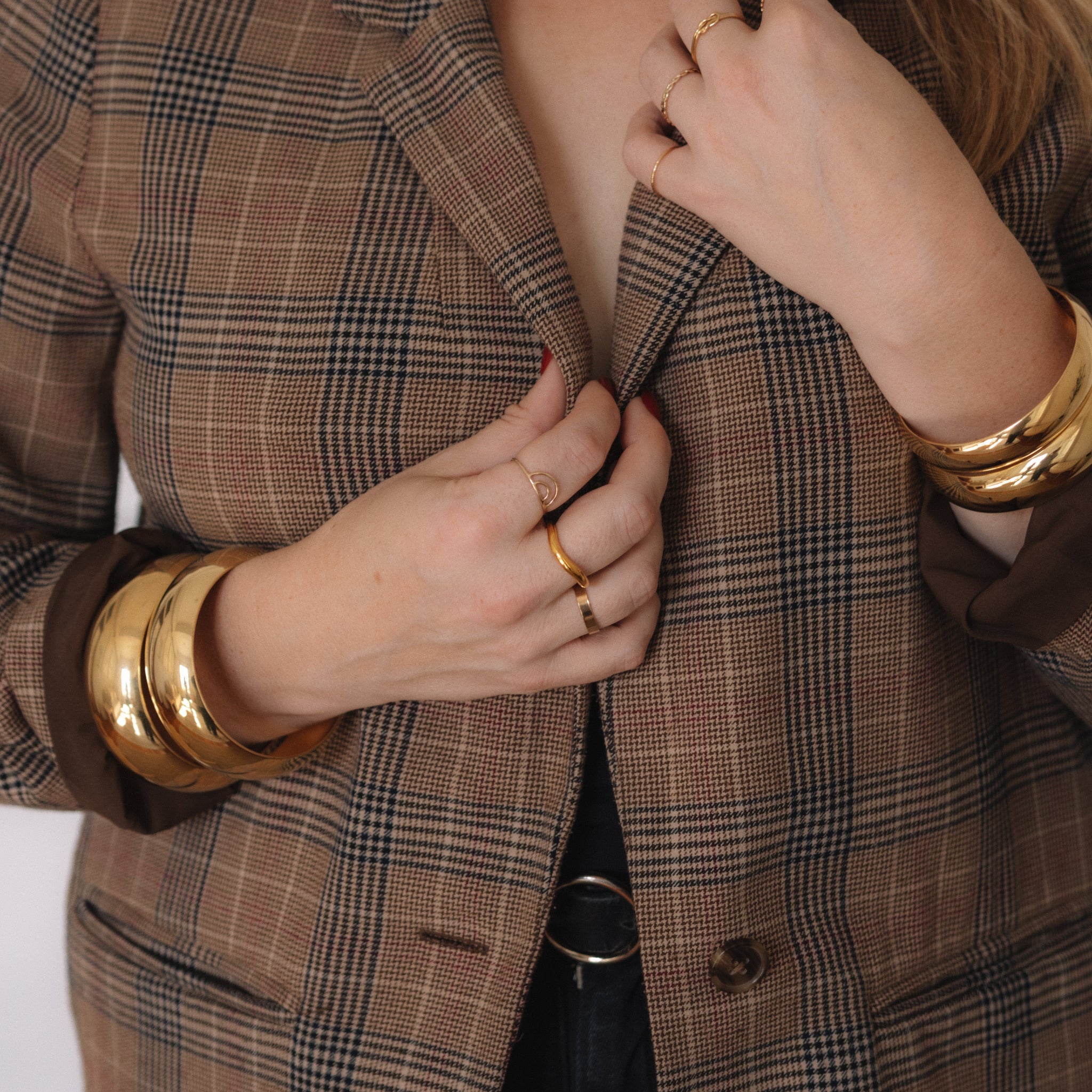 Person wearing a brown plaid blazer with gold jewelry on a white background
