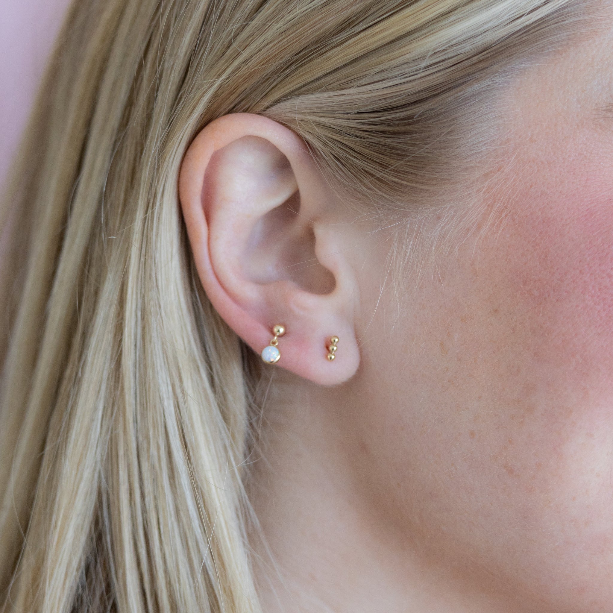 Close-up of an ear wearing gold and pearl earrings against a pink background