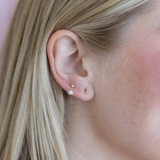 Close-up of an ear wearing gold and pearl earrings against a pink background