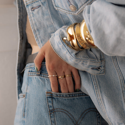 Person wearing a light blue denim jacket and jeans with gold jewelry.