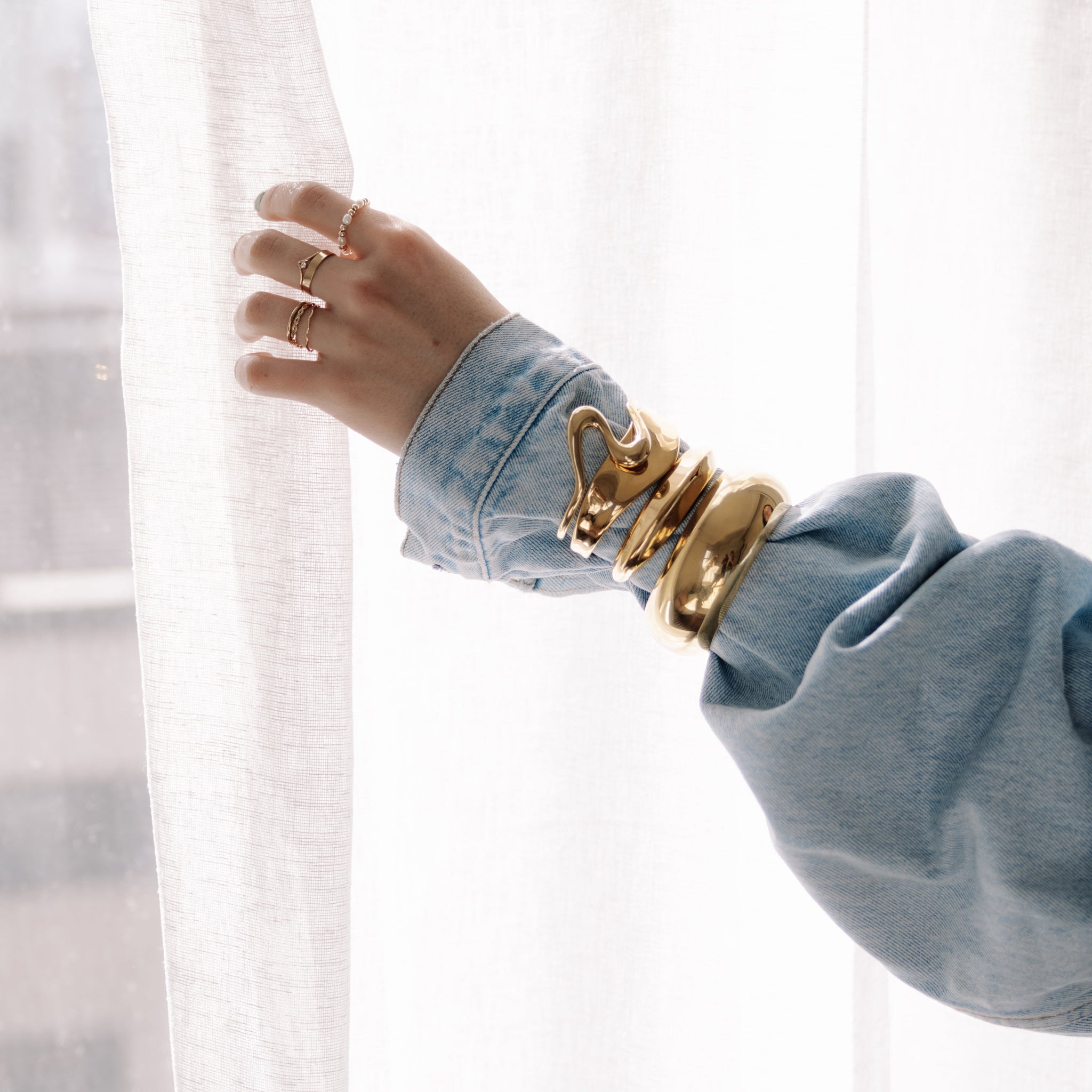 Hand wearing a gold bracelet with denim outfit. 