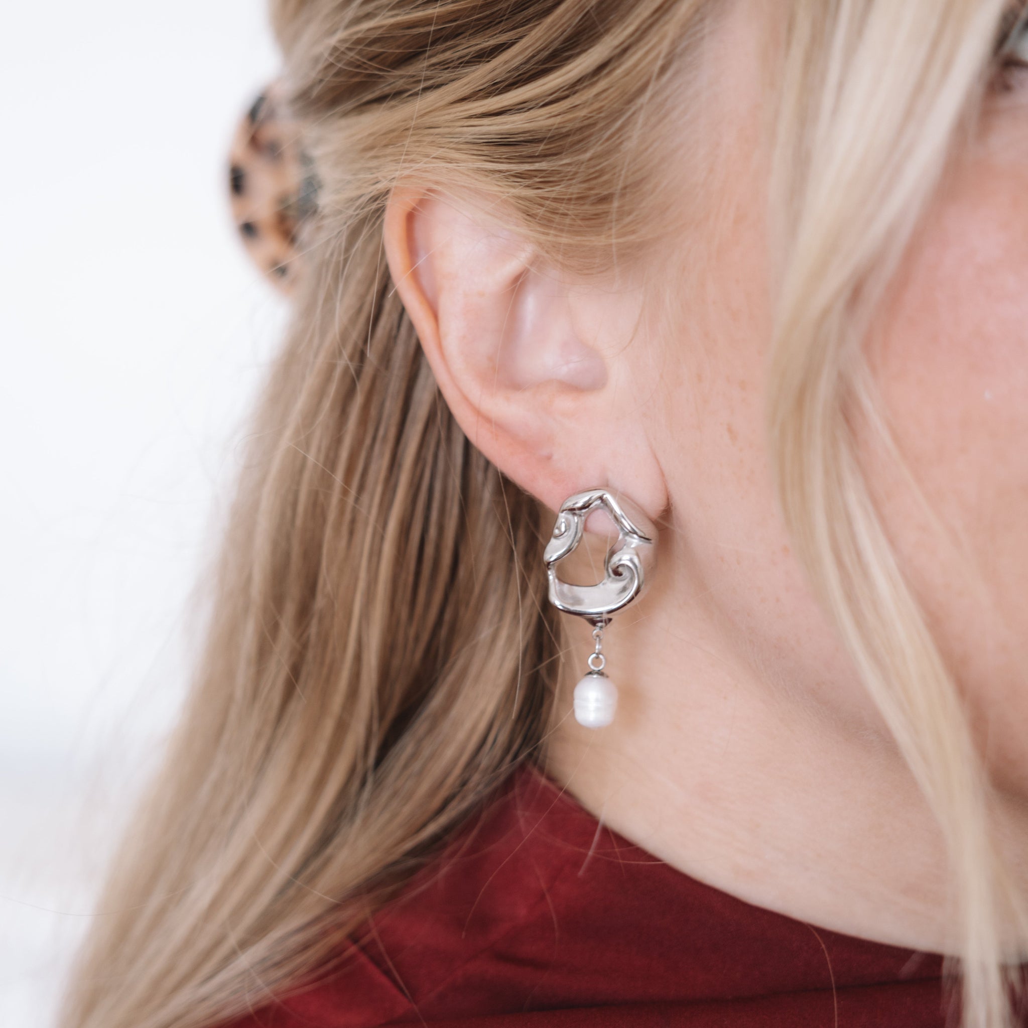 Close-up of a woman wearing a silver earring with a pearl on a blurred background