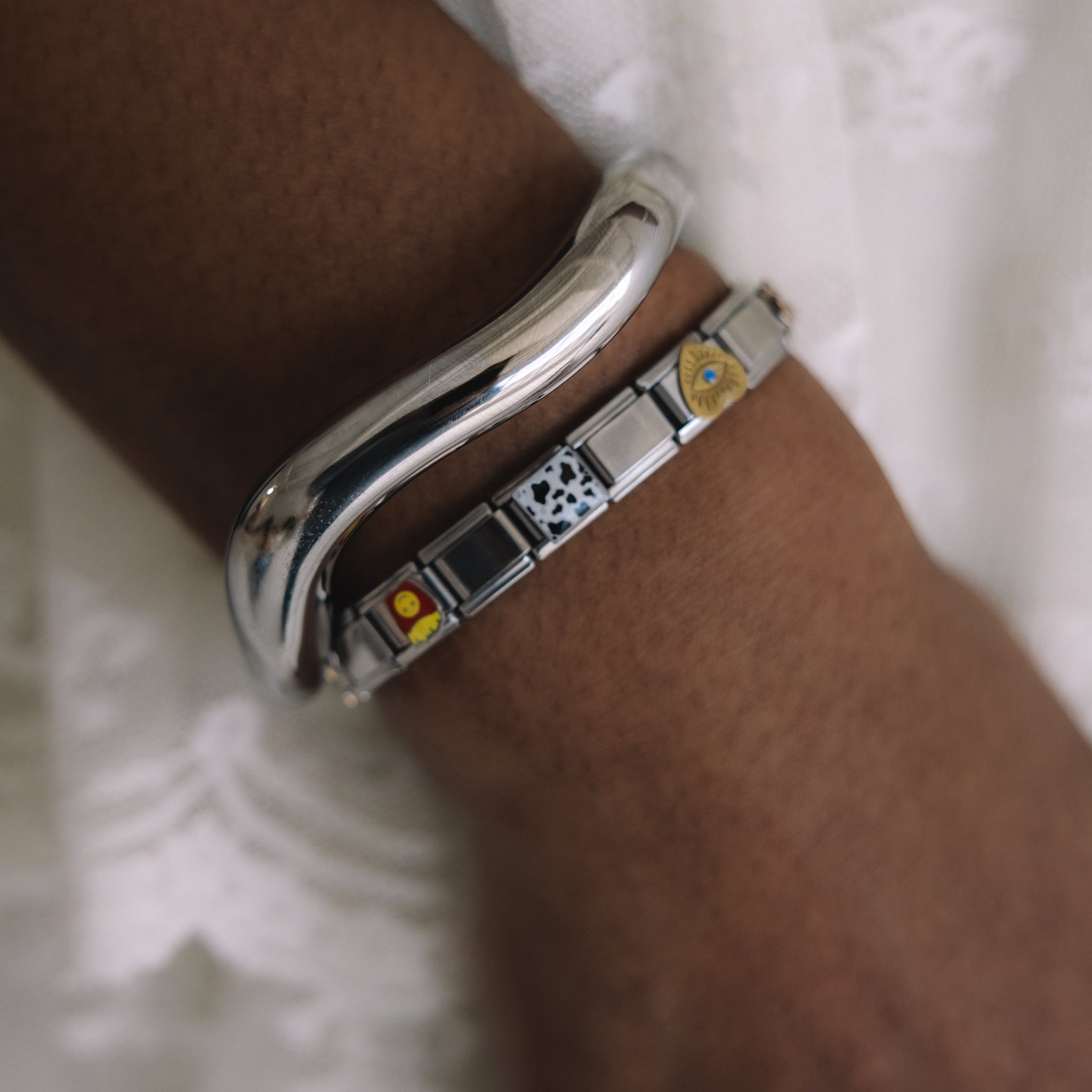 Silver bracelet with embedded stones on a wrist against a white lace background