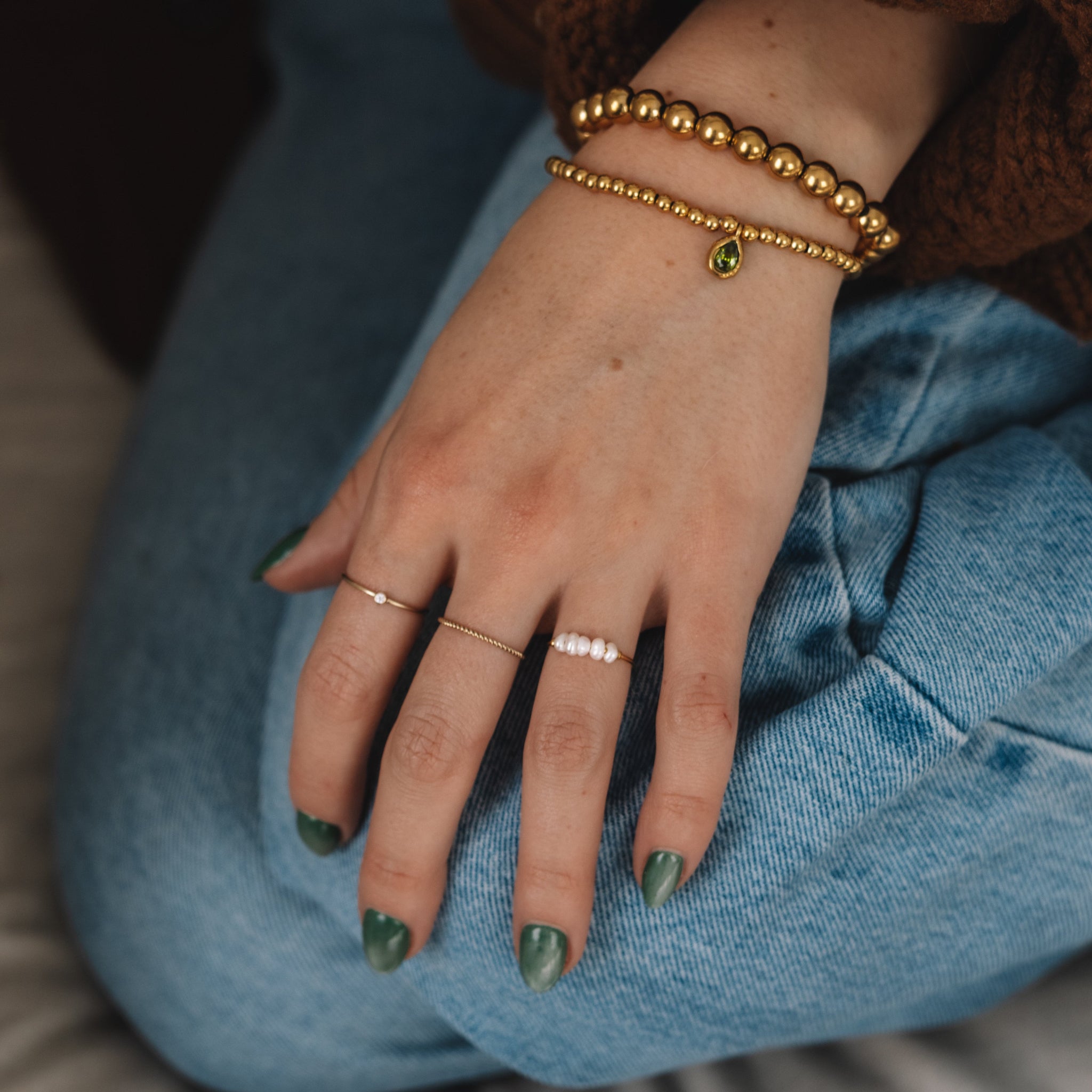 Hand with green nail polish wearing gold bracelets on a blue cushion.