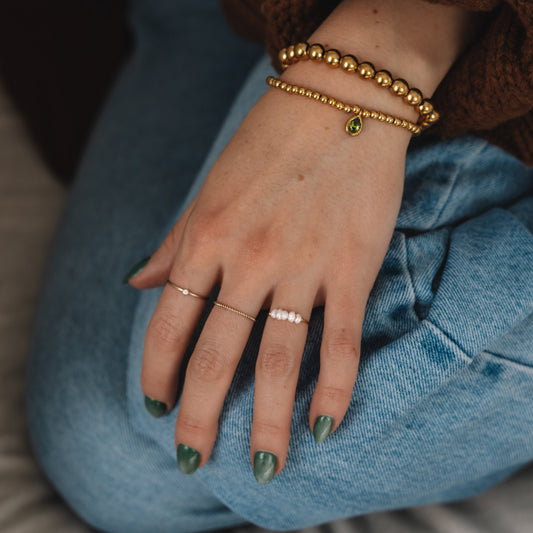 Hand with green nail polish wearing gold bracelets on a blue cushion.