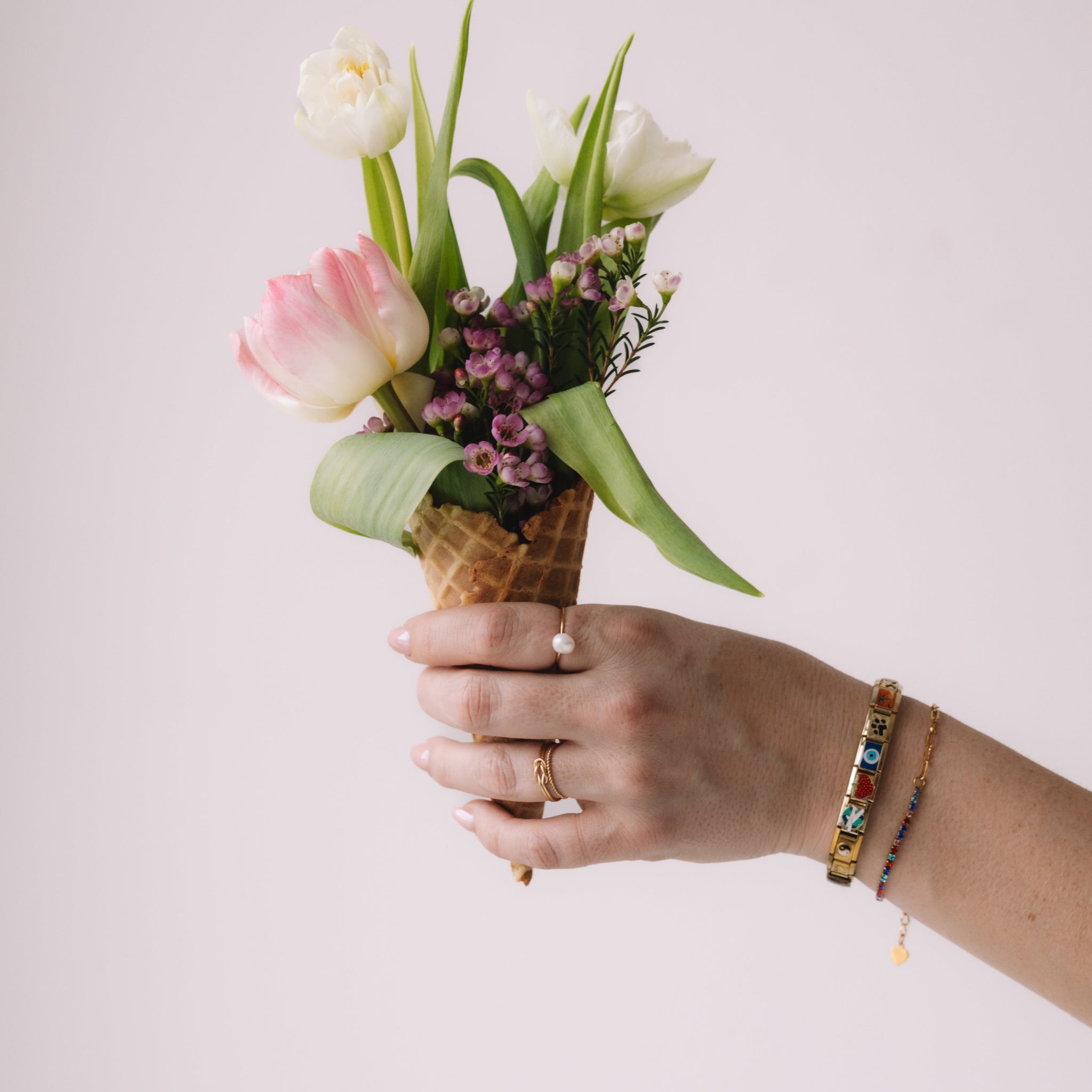 Hand holding a bouquet of flowers in an ice cream cone against a plain background