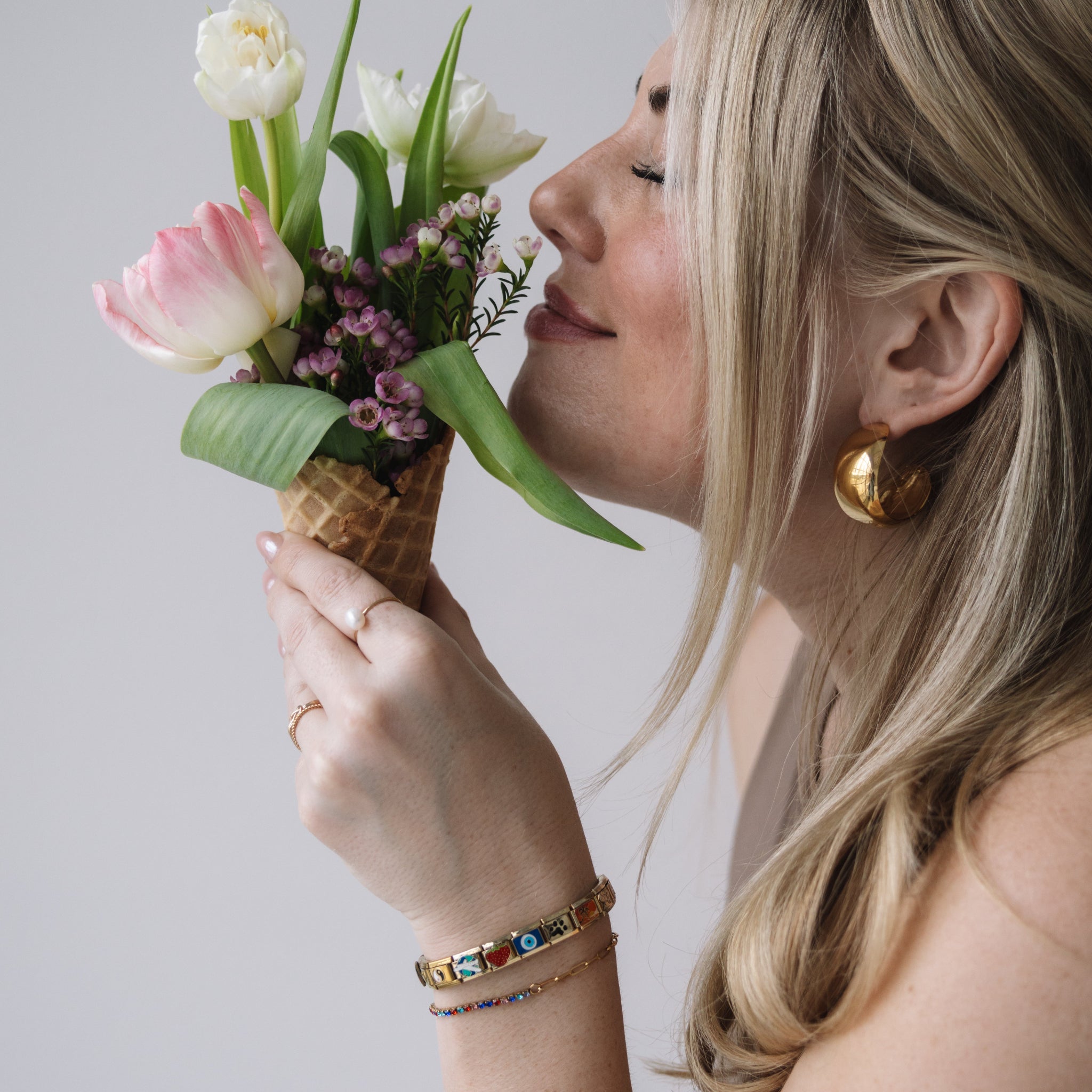 Woman holding a small bouquet of flowers in a cone-shaped container against a plain background