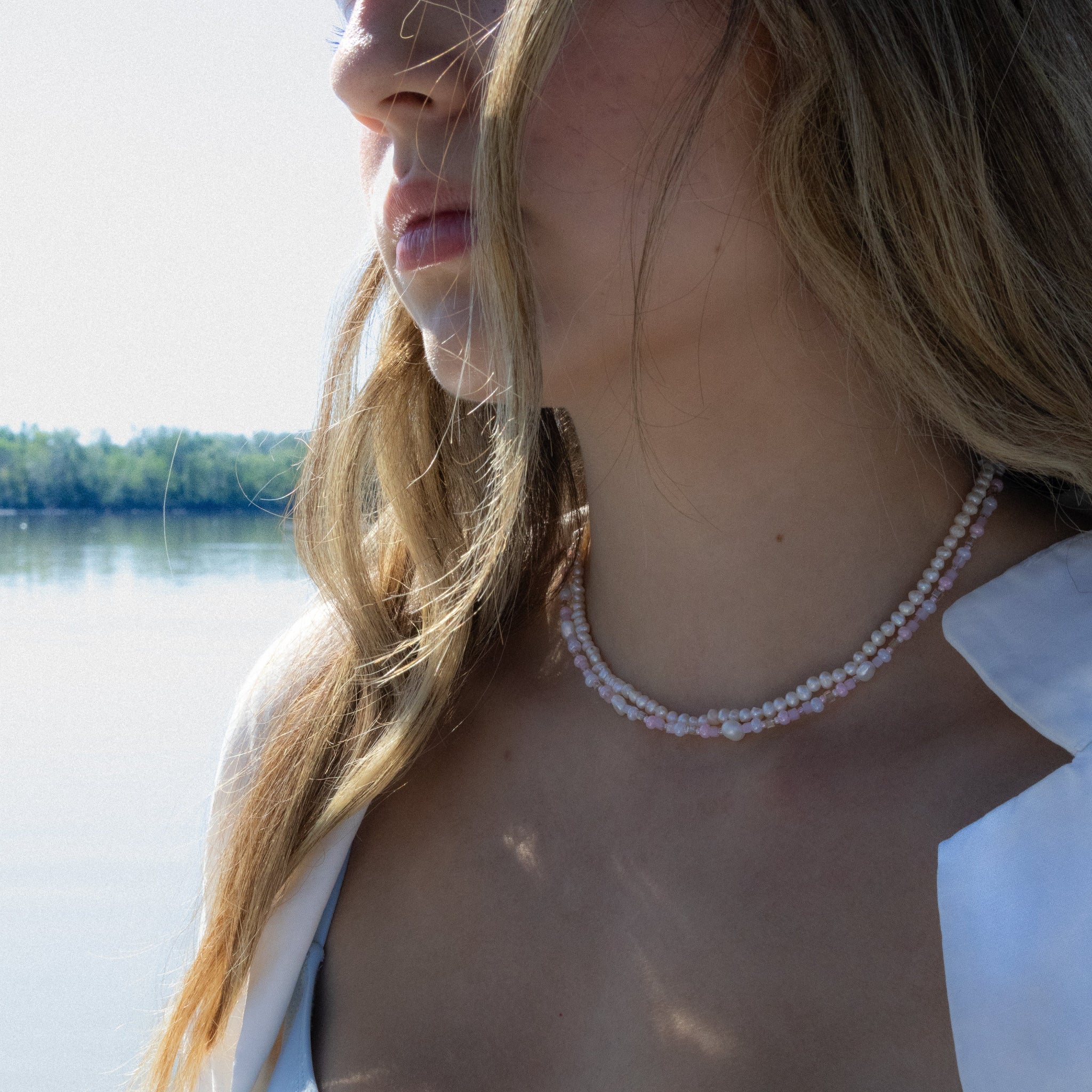 Woman wearing a blue bikini and pearl necklace by a body of water