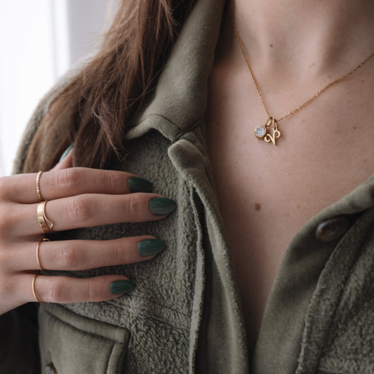 Person wearing a gold necklace with a pendant, green jacket, and green nail polish.