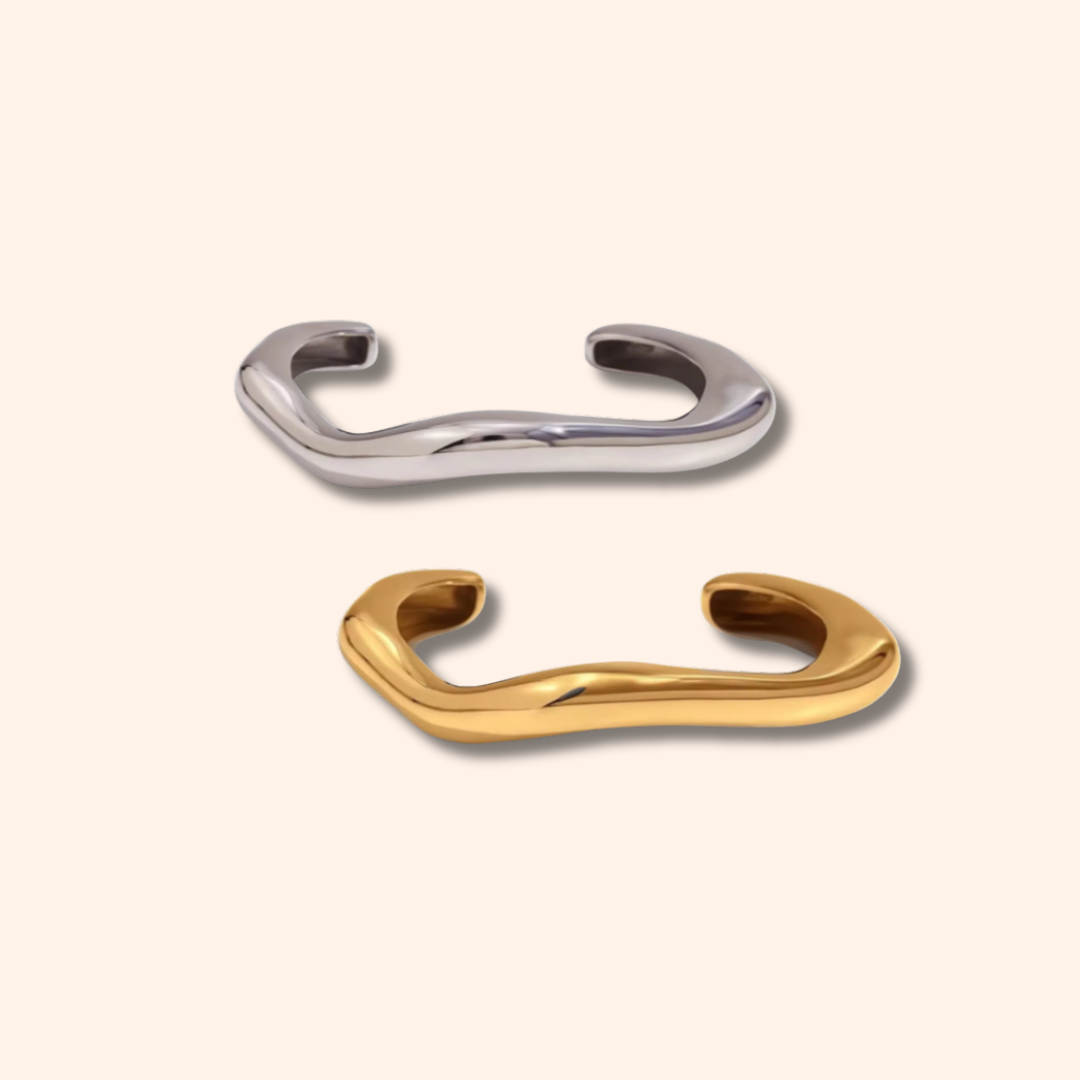 Two metallic bracelets, one silver and one gold, on a light beige background.