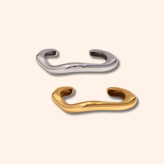 Two metallic bracelets, one silver and one gold, on a light beige background.