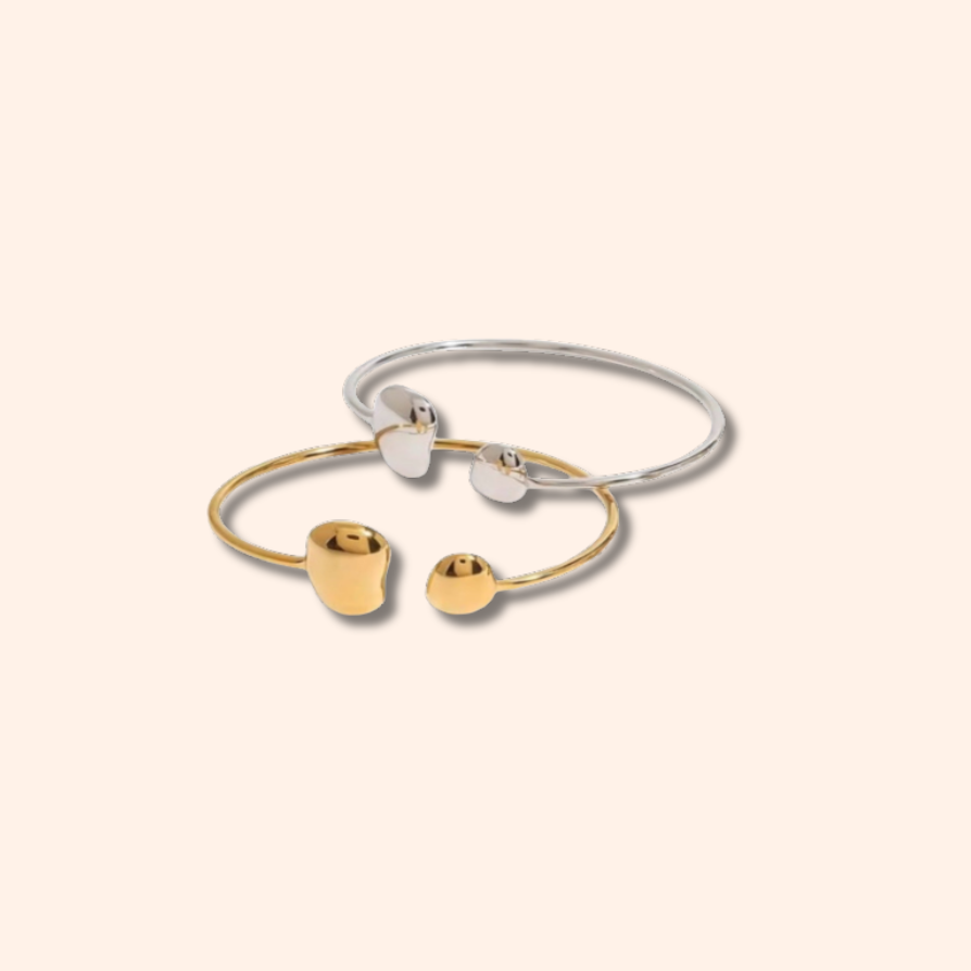 Two bracelets, one gold and one silver, on a light beige background