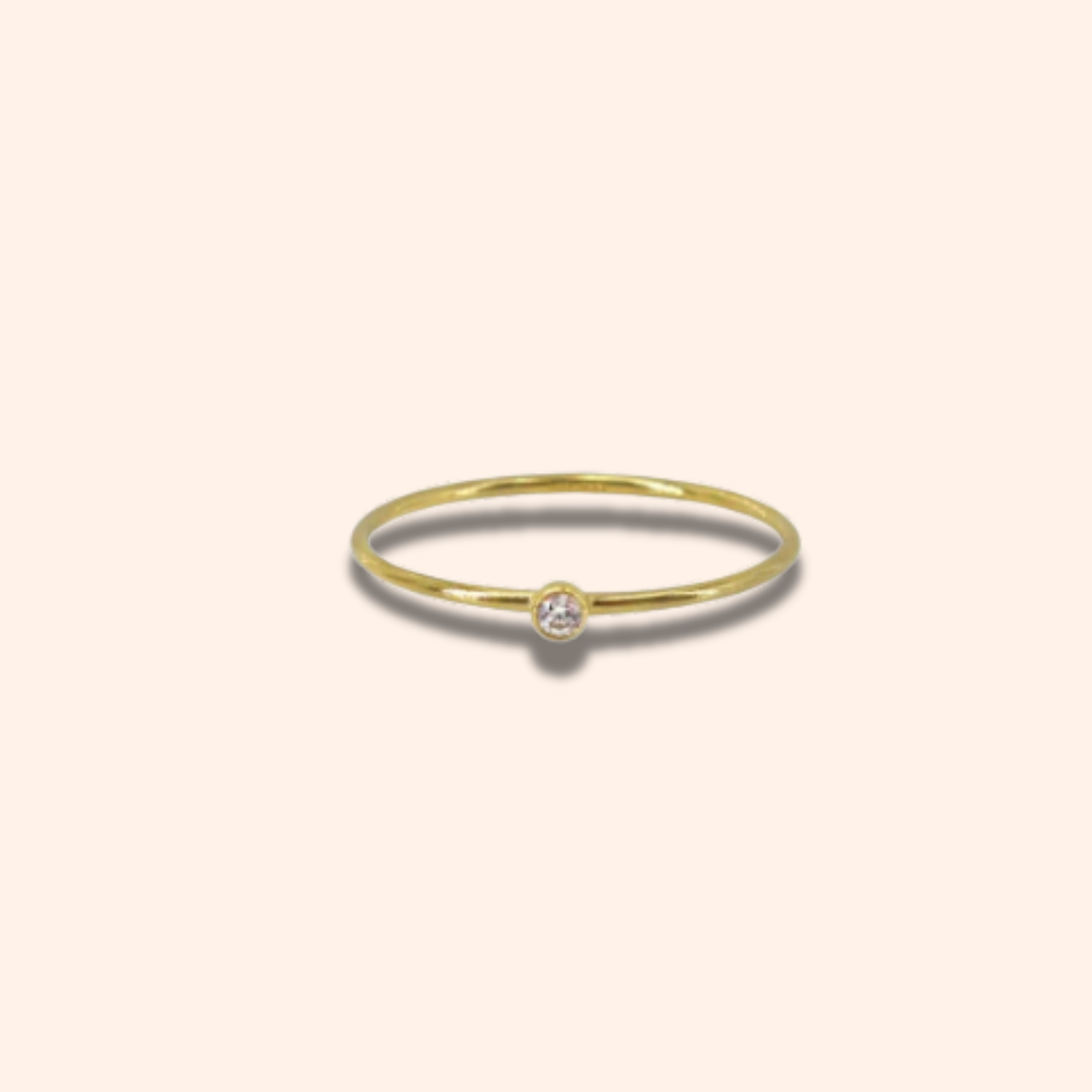 Gold ring with a small diamond on a light beige background