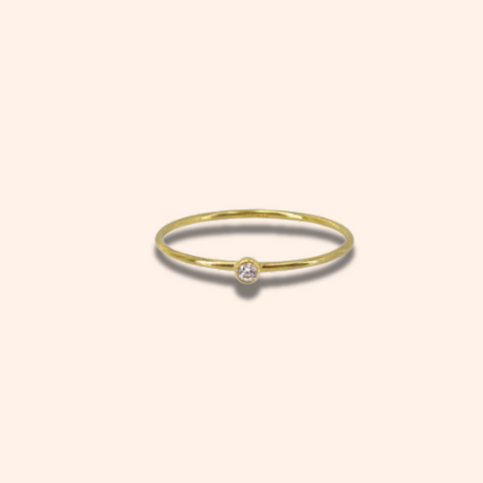 Gold ring with a small diamond on a light beige background