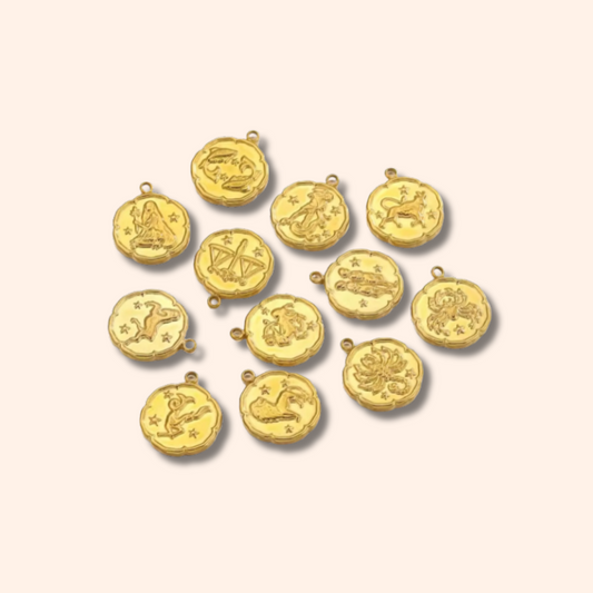 Gold pendants with zodiac symbols on a beige background