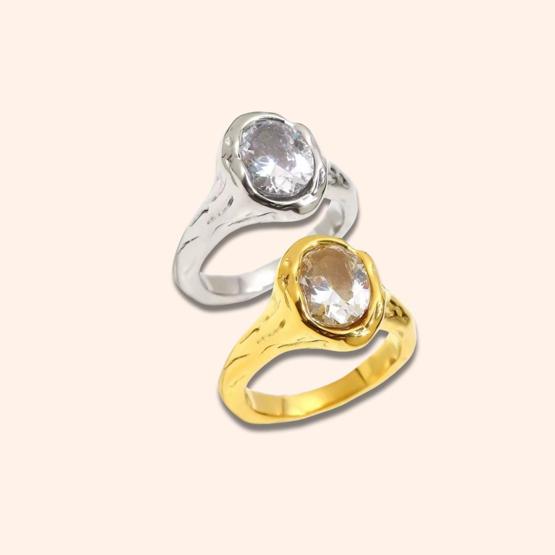 Two rings, one silver and one gold, with clear gemstones on a light beige background.