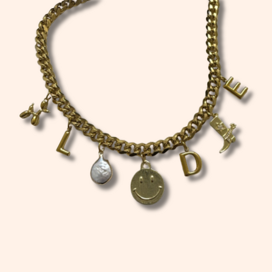 Gold chain bracelet with various charms on a light beige background