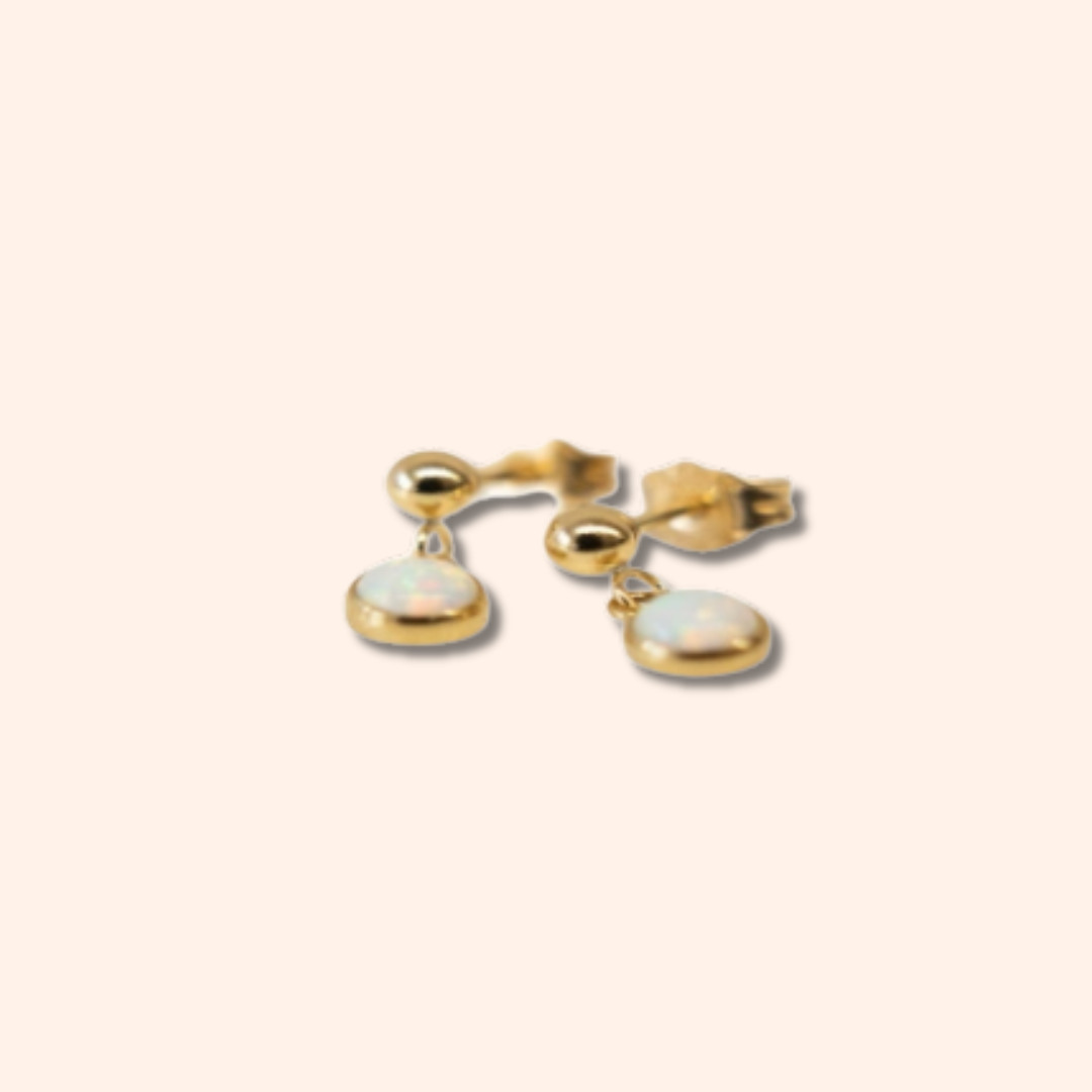 Gold earrings with opal stones on a beige background