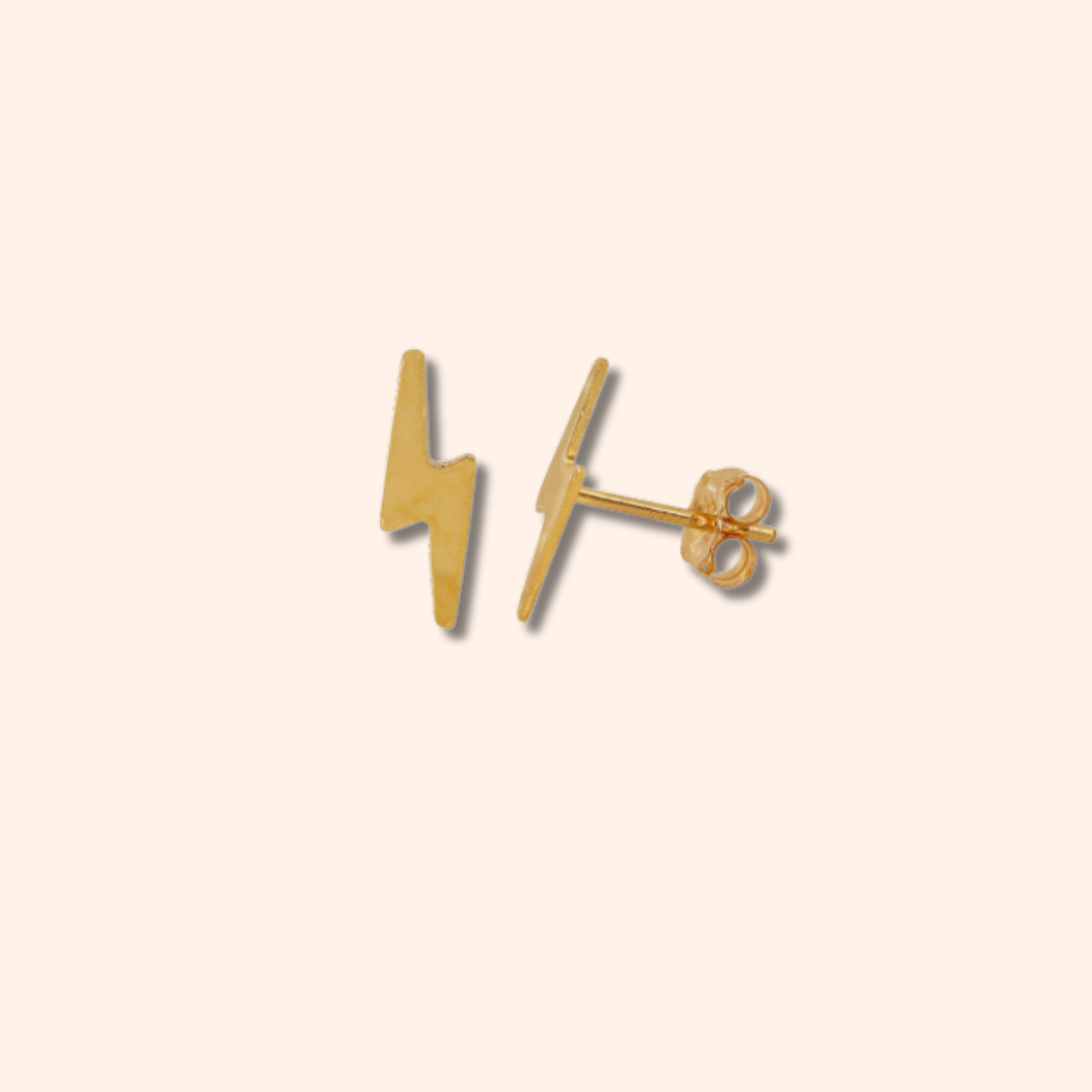 Gold lightning bolt stud earrings on a beige background