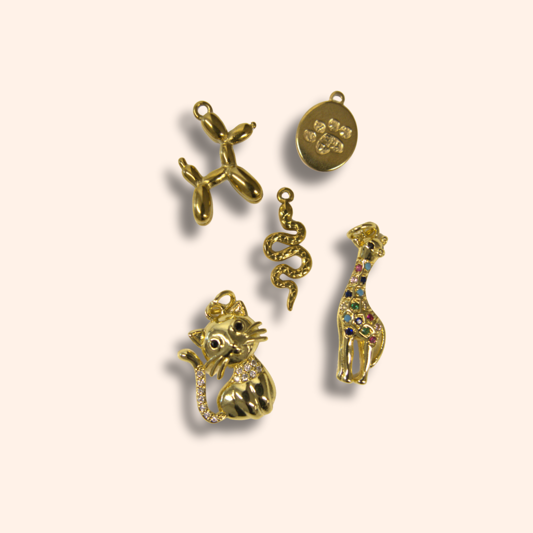 Gold charms including a balloon dog, snake, cat, and giraffe on a beige background