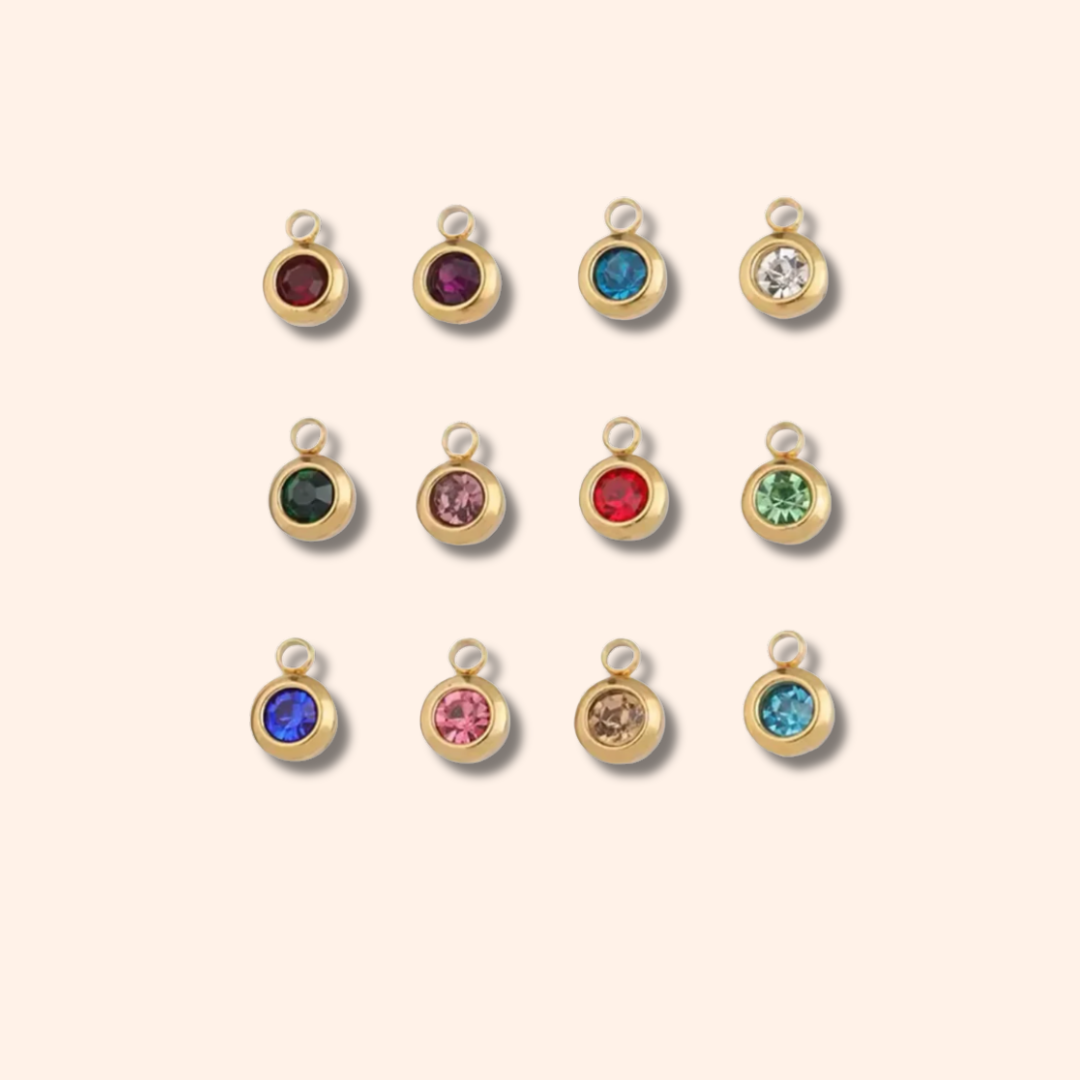 Set of gold charm pendants with colorful gemstones on a beige background