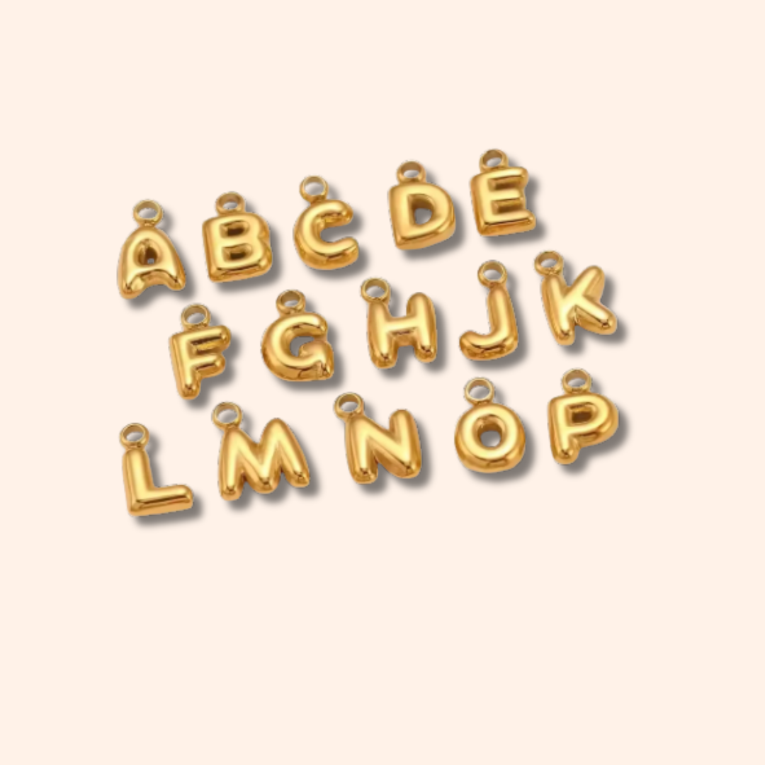 Gold letter charms spelling 'ABCDEFGHIJKLMOP' on a beige background