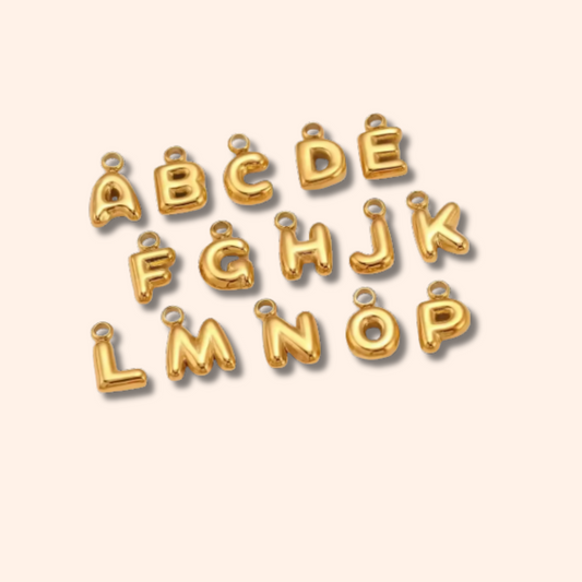 Gold letter charms spelling 'ABCDEFGHIJKLMOP' on a beige background