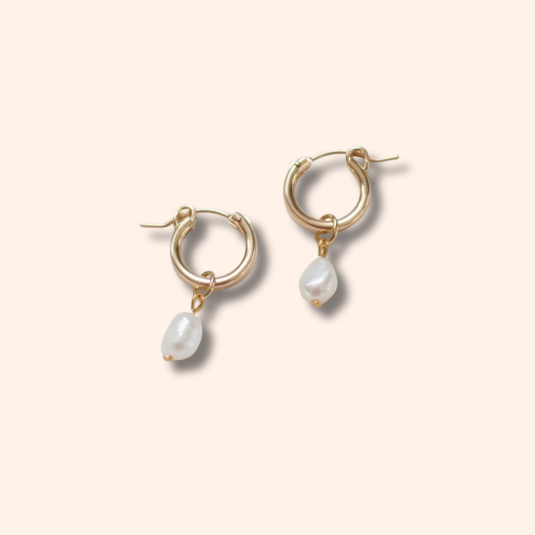 Gold hoop earrings with pearl drops on a beige background