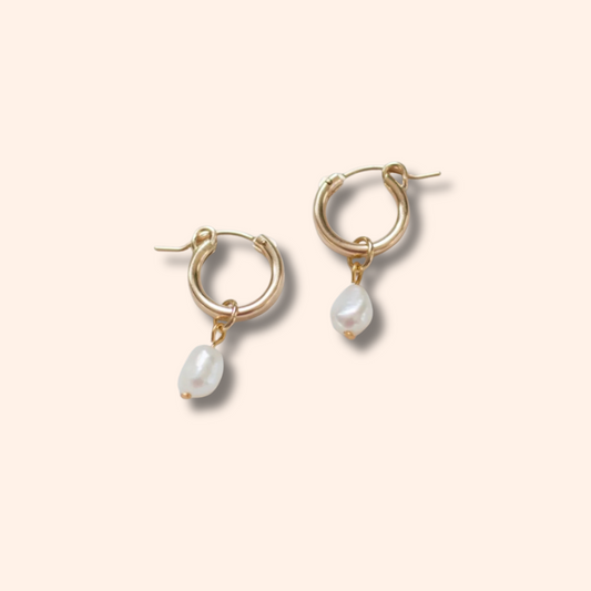 Gold hoop earrings with pearl drops on a beige background