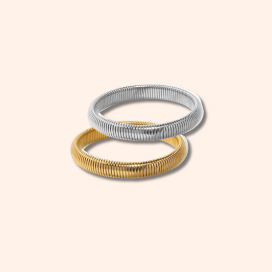 Two metallic bracelets, one gold and one silver, on a light beige background.